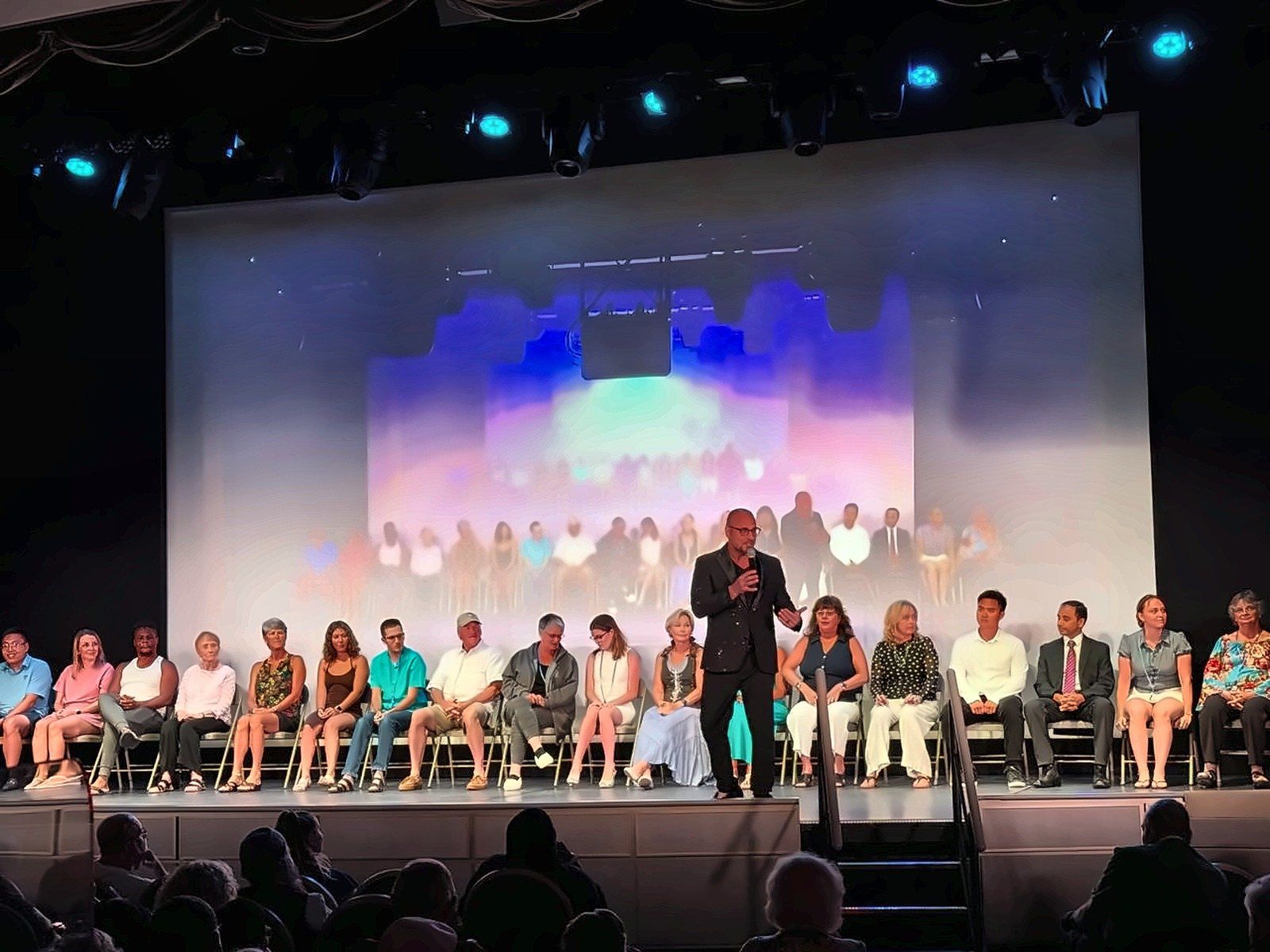 Eric Mina on stage with a full row of adult volunteers