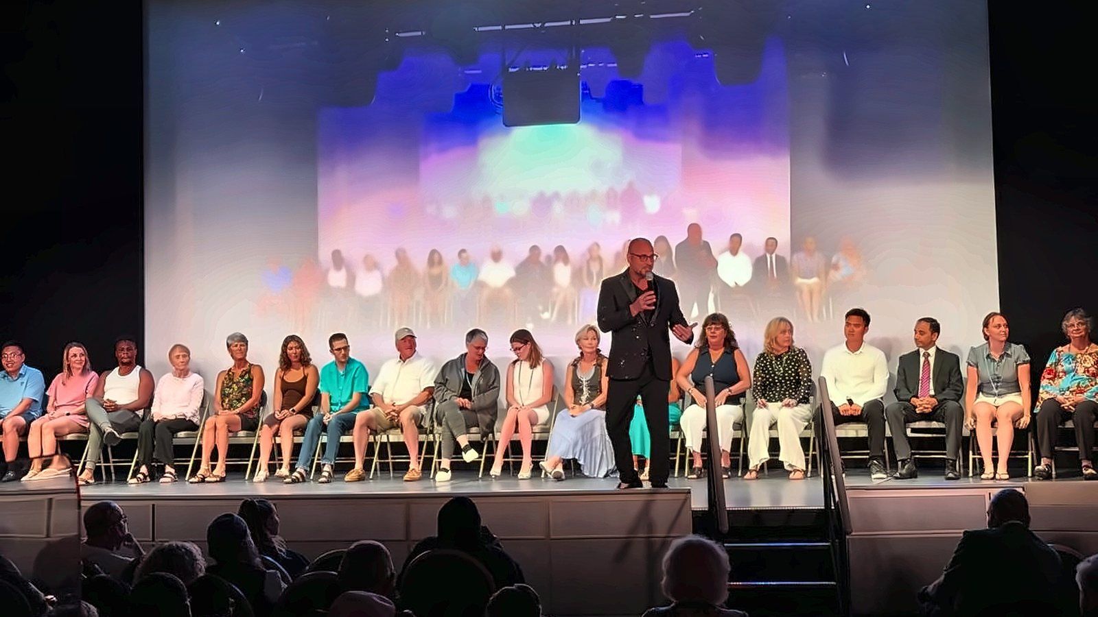 Eric Mina on stage with a full row of adult volunteers